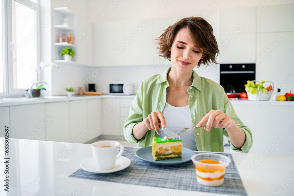 Photo of adorable charming lady dressed green shirt enjoying tasty sweet dessert indoors house kitchen Photo of adorable charming lady dressed green shirt enjoying tasty sweet dessert indoors house kitchen