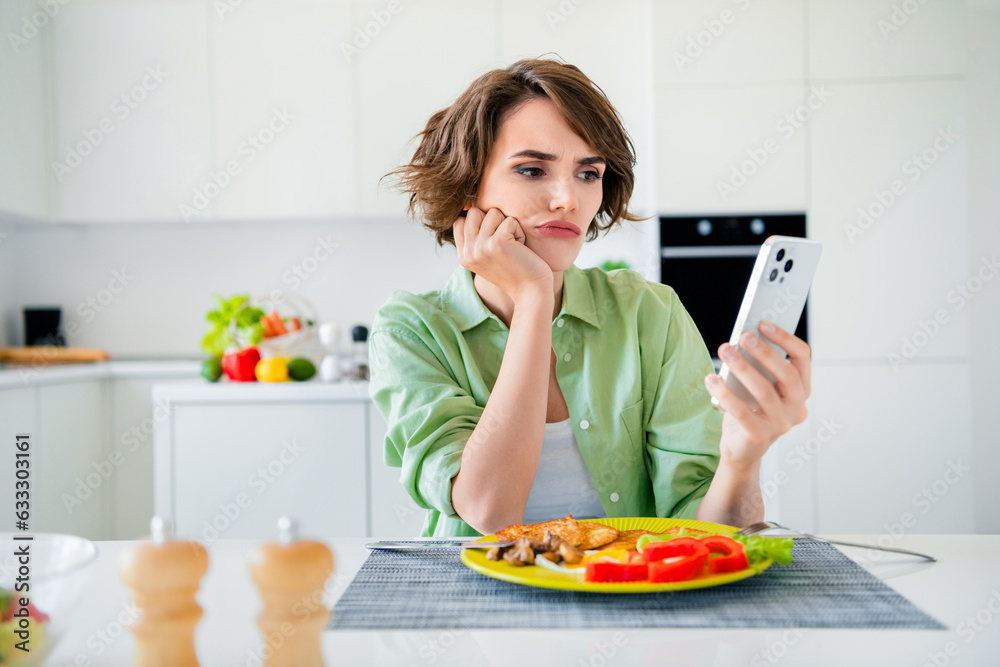 Photo of stressed bored lady dressed green shirt texting modern device eating dinner indoors house kitchen