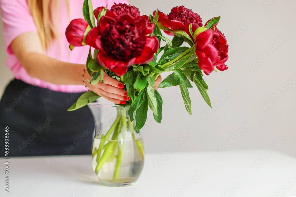 Woman, florist put a peonies in a vase. Beautiful pink pions peonies in a jar. Close up.