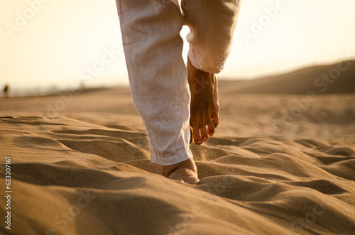 Feet of a man walking through the desert dunes during the sunset photo