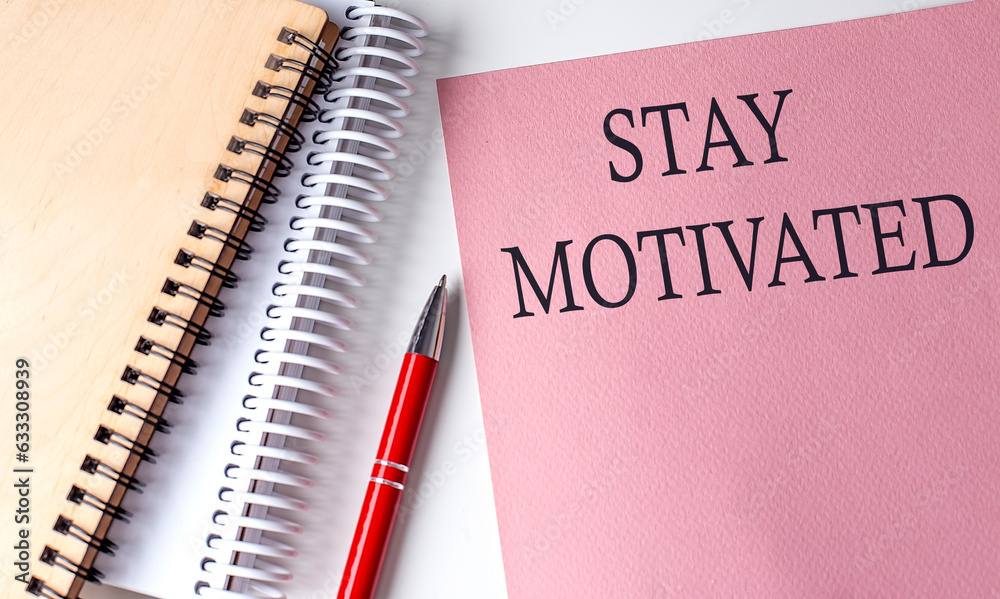 STAY MOTIVATED word on the pink paper with office tools on white background STAY MOTIVATED word on the pink paper with office tools on white background
