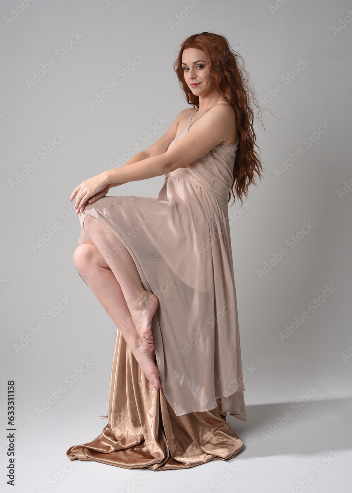 Full length portrait of beautiful female model with long brunette hair wearing a creamy pink gown dress. graceful sitting pose isolated on white studio background. Full length portrait of beautiful female model with long brunette hair wearing a creamy pink gown dress. graceful sitting pose isolated on white studio background.