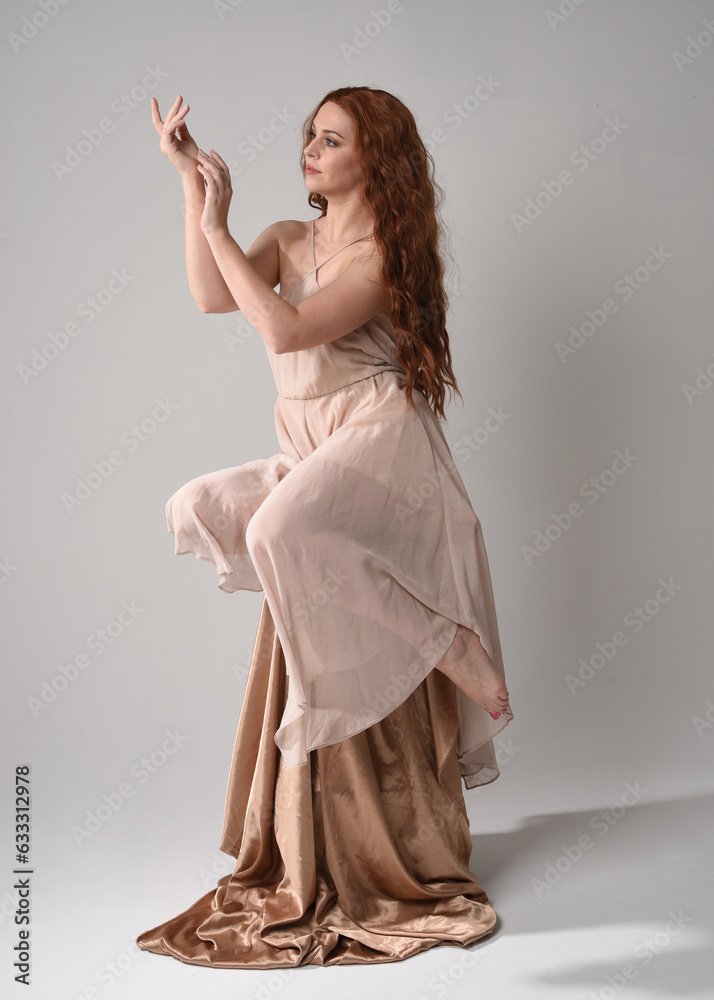 Full length portrait of beautiful female model with long brunette hair wearing a creamy pink gown dress. graceful sitting pose isolated on white studio background. Full length portrait of beautiful female model with long brunette hair wearing a creamy pink gown dress. graceful sitting pose isolated on white studio background.