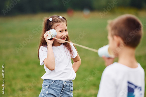 String can phone in hands, talking. Boy and girl are together having fun on the field at daytime