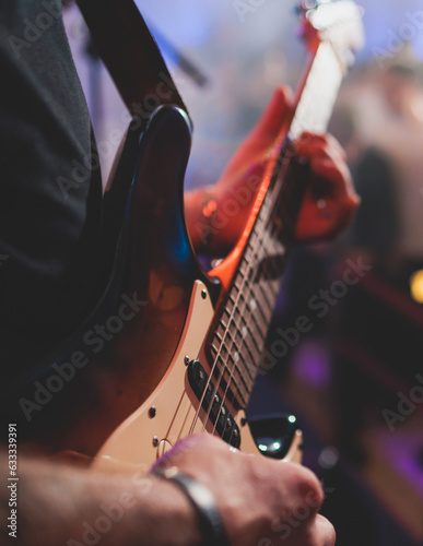 Concert view of an electric guitar player with vocalist and rock band performing in a club, male musician guitarist on stage with audience in a crowded concert hall arena