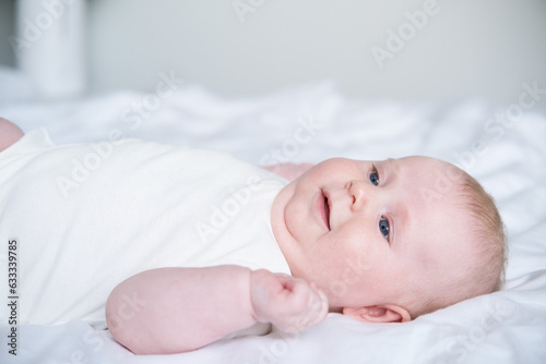 healthy smiling baby lies on his back on bed on white bedding