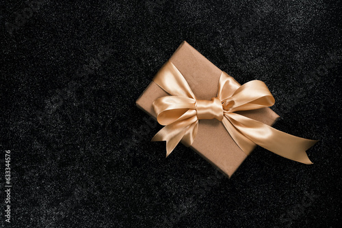 Beautiful box with a gift on a black table. Gift with a golden bow, from above.