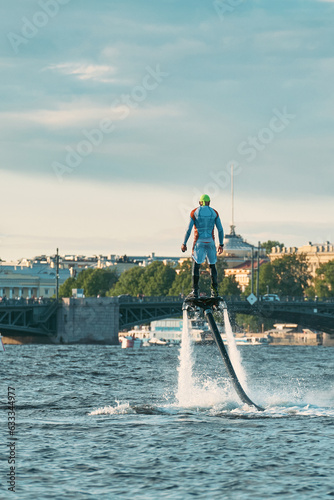 A man takes off above the water on a flyboard in the city river. A sportsman is engaged in an extreme sport, rising into the air due to a water jet. photo