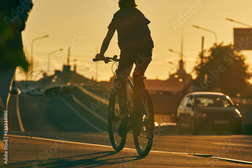 Silhouette of a man on a bicycle. A cyclist rides along the sidewalk through the city at sunset, backlight.