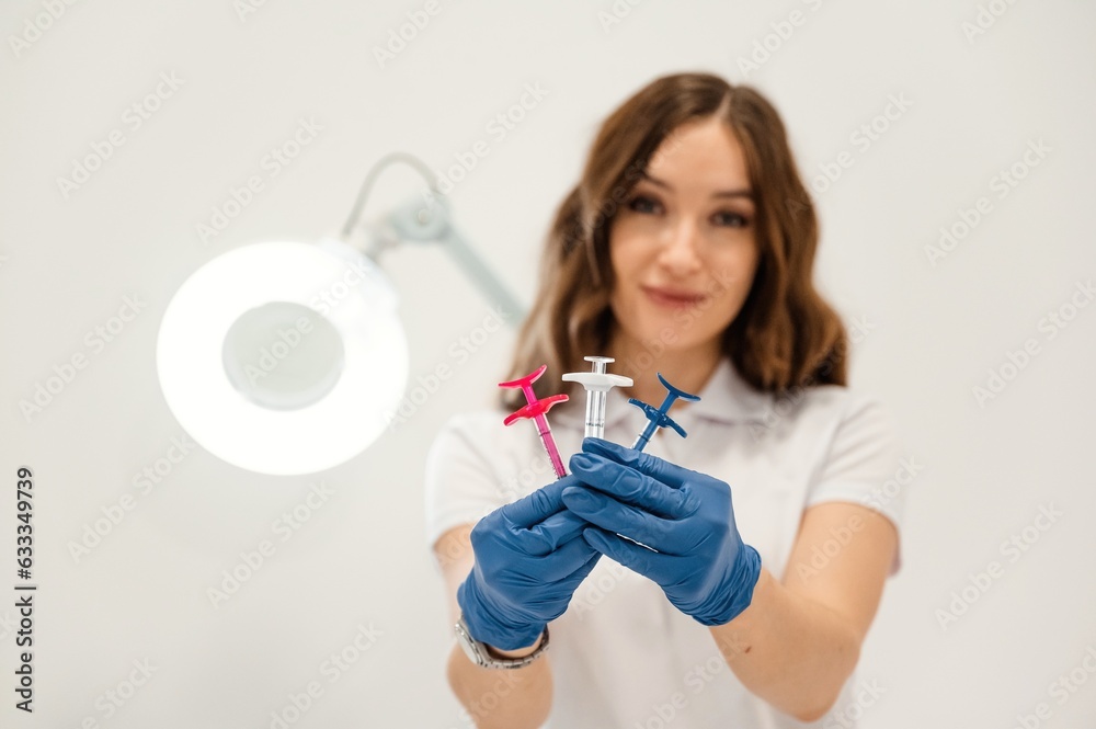 White wall. Cosmetologist holding syringes for injection lips augmentation. Women's cosmetology in the beauty salon White wall. Cosmetologist holding syringes for injection lips augmentation. Women's cosmetology in the beauty salon