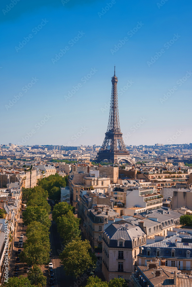 Sunny day view of the Eiffel Tower in Paris, France, surrounded by trees under a clear blue sky.