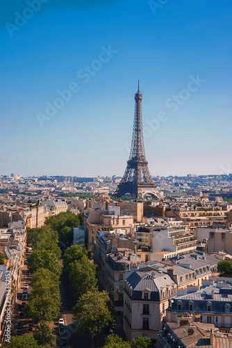 Sunny day view of the Eiffel Tower in Paris, France, surrounded by trees under a clear blue sky.