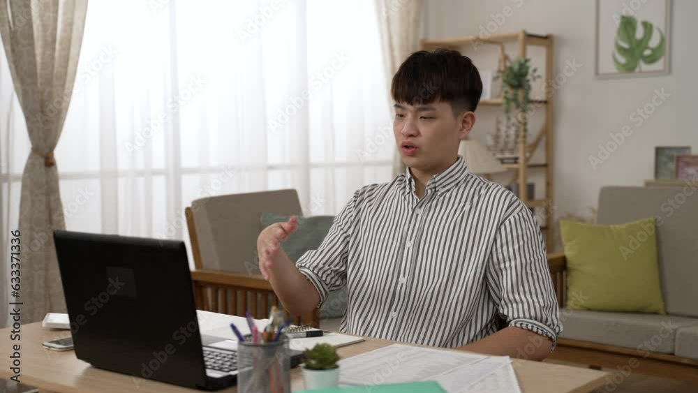 asian businessman working from home is expressing ideas with hand gestures while having a conference call on the laptop in a modern living room asian businessman working from home is expressing ideas with hand gestures while having a conference call on the laptop in a modern living room