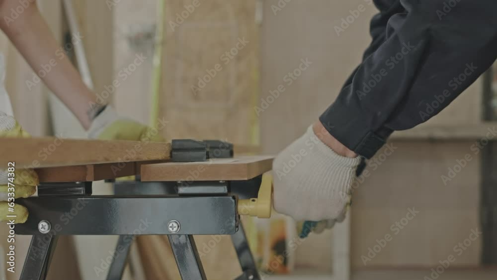 Cropped shot of two unrecognizable repairmen adjusting portable woodworking workbench while working together on construction site indoors Cropped shot of two unrecognizable repairmen adjusting portable woodworking workbench while working together on construction site indoors