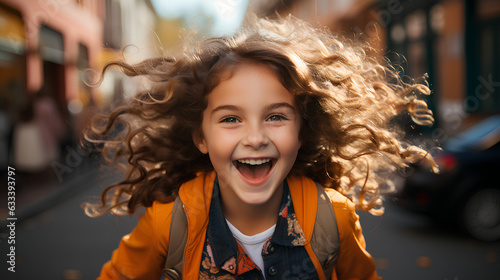 cheerful little girl with flying hair smiling at camera on street