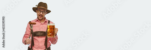Banner. Attractive bavarian man wearing traditional fest outfit holding huge beer mug and appertizing fried sausage. Oktoberfest concept