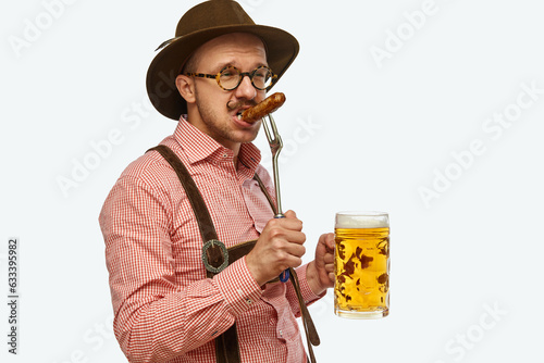 Attractive bavarian man wearing traditional fest outfit holding huge beer mug and bites hot fried sausage. Oktoberfest concept