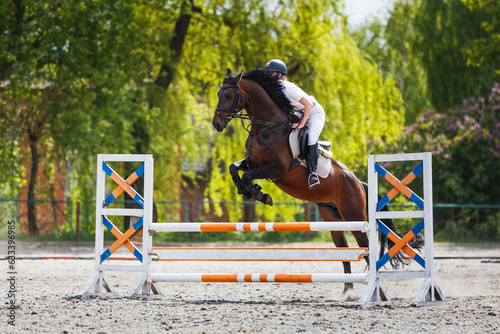 Young female rider jumping over obstacle on her show jumping competition