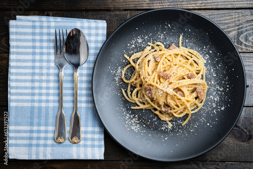 Spaghetti carbonara, traditional Italian pasta dish served on a plate on a dark wooden table