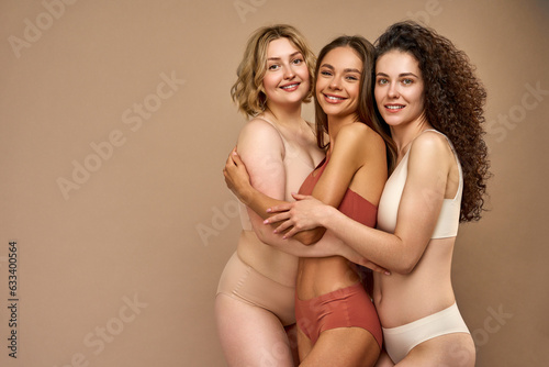 Three confident beautiful different adult women posing together in comfortable underwear standing on a beige background. Self-acceptance and self-love. Healthy and glowing skin. Copy space.