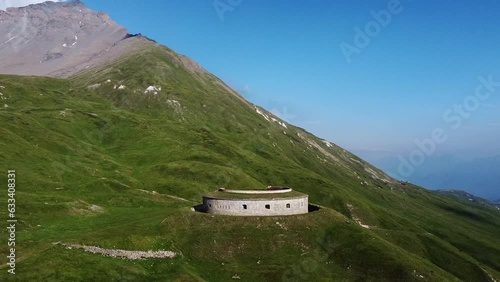 Panoramic aerial drone view of round fortification called Fort de Ronce, Alps mountains and Mont Cenis lake, Val Cenis, Savoie, France. Bird eye view of old military fort overgrown with green grass  photo