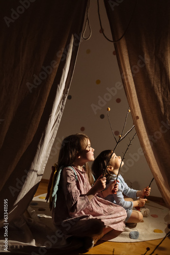 Kids sitting and playing on mat behind tent indoors