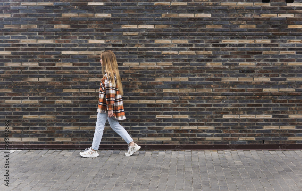 young woman walks down the street against a brick wall young woman walks down the street against a brick wall