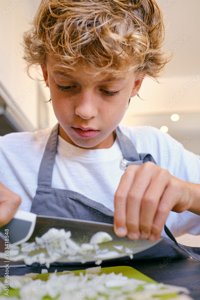 Crop attentive boy cutting raw onion in house kitchen Crop attentive boy cutting raw onion in house kitchen
