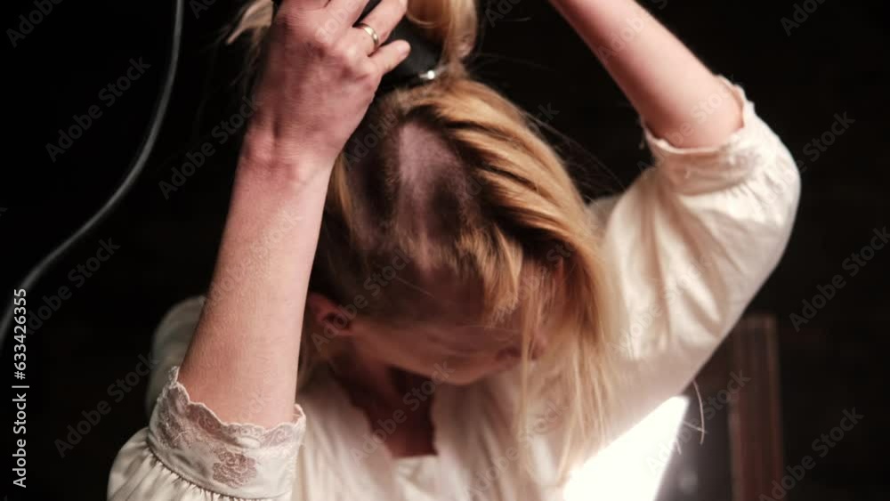Cutting long hair of a woman with a clipper. A middle-aged woman cuts her hair in a dark room.