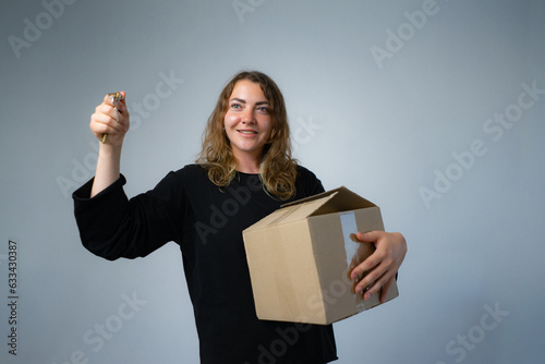 Happy woman moving in carrying cartons boxes with red paper house and key. Young girl arranging interior and unpacking at new apartment home. photo