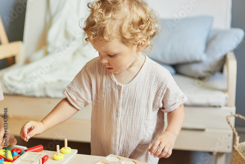 Playful kindergarten games. Educational toy for toddlers. Happy preschool learning. Curious wavy haired blonde infant baby playing wooden educational toys at home interior.