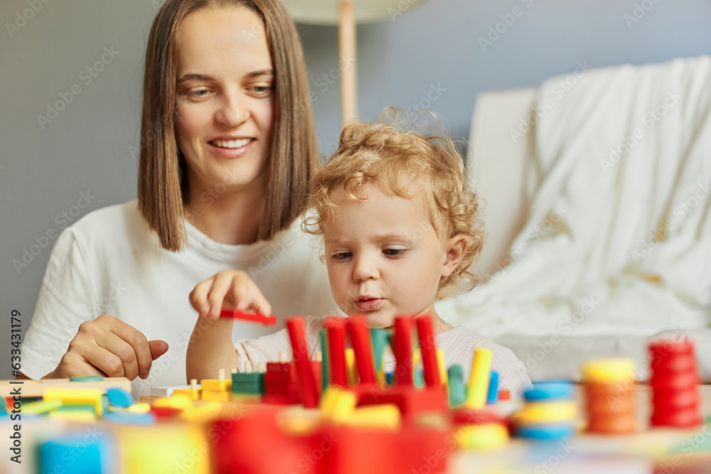 Babysitter's playful care. Exploring together in the nursery. Happy family leisure time. Joyful mother playing with little baby daughter engaged in game activity at home interior Babysitter's playful care. Exploring together in the nursery. Happy family leisure time. Joyful mother playing with little baby daughter engaged in game activity at home interior