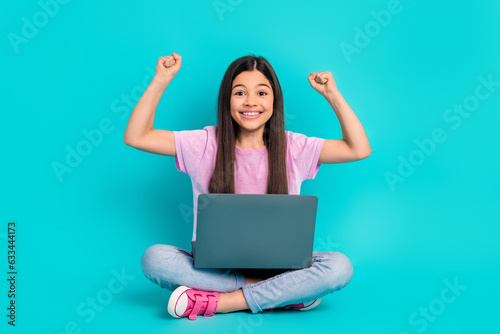 Full body photo cadre of small cute schoolgirl fists up enjoy playing computer games online victory isolated on cyan color background © deagreez