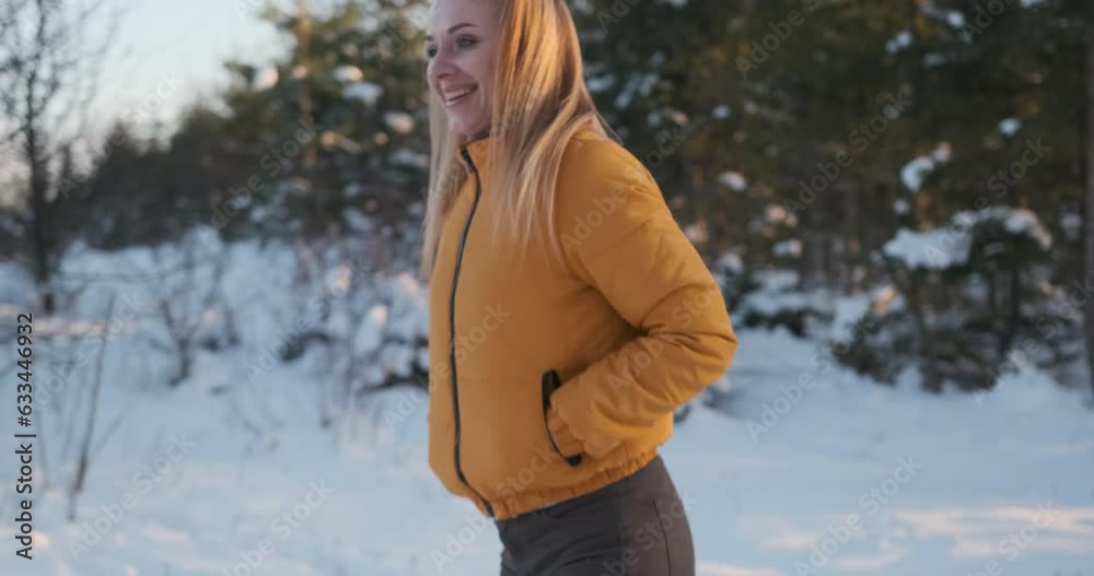 Energetic woman has fun in winter in nature. Cheerful girl in bright orange jacket jumps and dances in snow on forest or park background Energetic woman has fun in winter in nature. Cheerful girl in bright orange jacket jumps and dances in snow on forest or park background