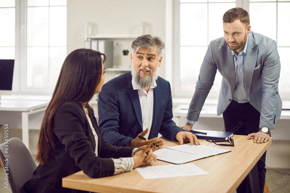 Group of three coworkers and employees on workplace at the desk discussing new project, reaching agreement and going signing a contract. Corporate business people having a meeting in office