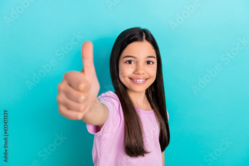 Photo of confident pretty little child dressed pink t-shirt showing thumb up isolated teal color background