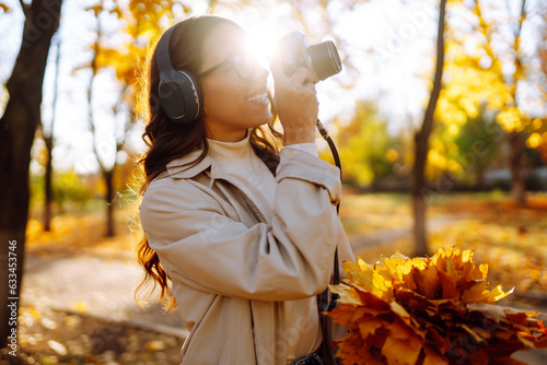 Smiling woman with retro camera and headphones enjoys sunny weather in autumn park. Autumn lifestyle.