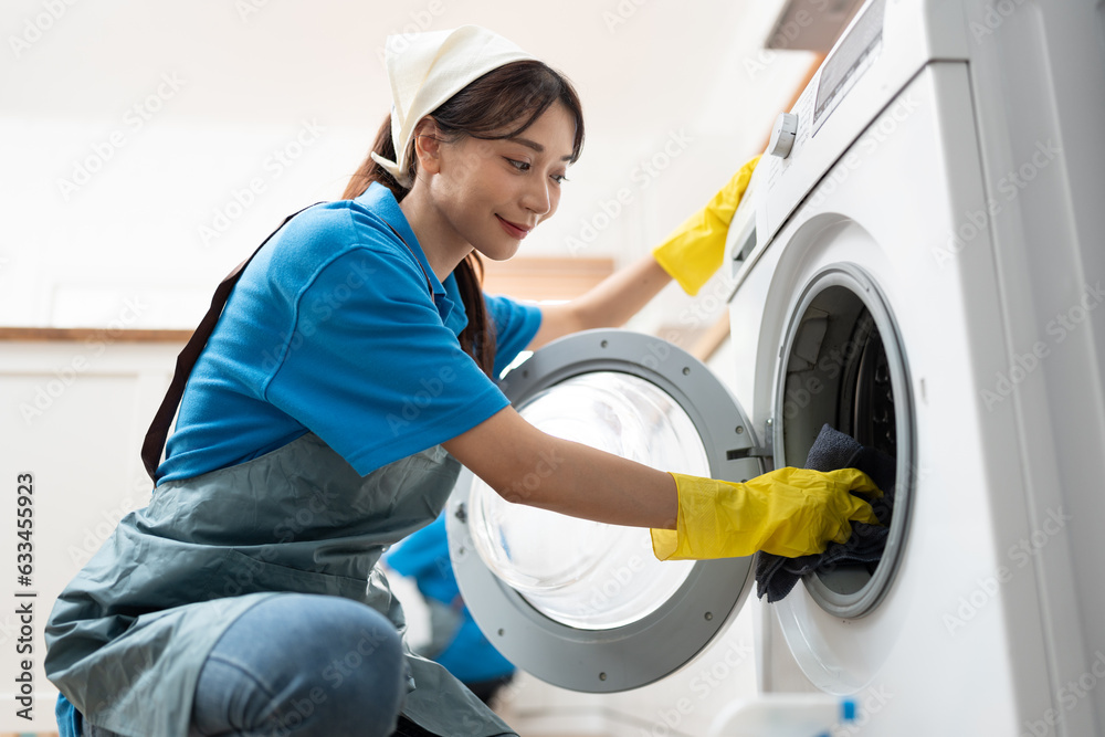 Asia woman in workwear maid cleaning home wiping with microfiber cloth to washing machine in kitchen room at home Asia woman in workwear maid cleaning home wiping with microfiber cloth to washing machine in kitchen room at home