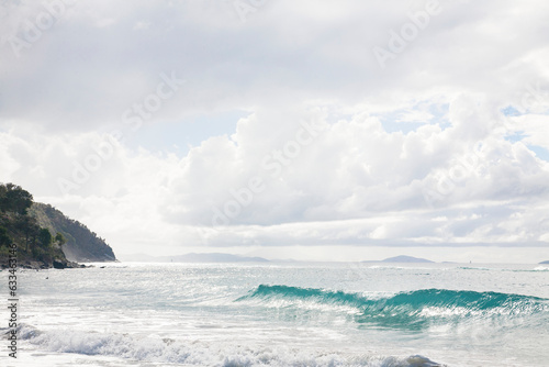 Turquoise wave and foamy surf rolling onto the shore against a pale grey  cloudy sky along the beach at Cane Garden Bay  Tortola  British Virgin Islands  Caribbean
