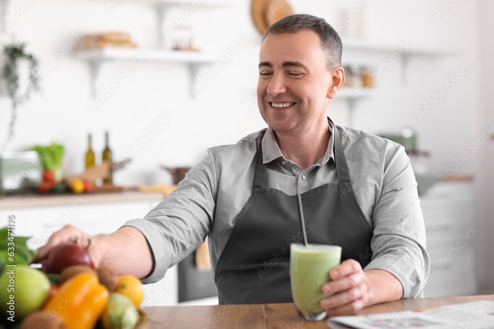 Mature man with glass of fresh smoothie and fruits in kitchen Mature man with glass of fresh smoothie and fruits in kitchen