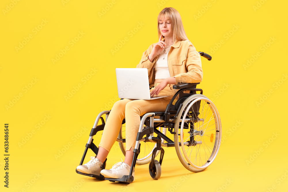 Young woman using laptop in wheelchair on yellow background Young woman using laptop in wheelchair on yellow background