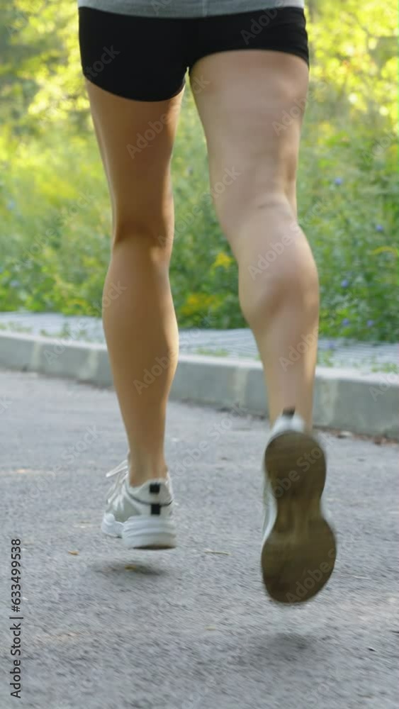 Vertical Screen: Slow motion legs of woman wearing shorts running on asphalt road in summer. Tracking shot partial view of female athlete training outside. Concept of fitness Vertical Screen: Slow motion legs of woman wearing shorts running on asphalt road in summer. Tracking shot partial view of female athlete training outside. Concept of fitness