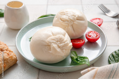 Plate of tasty Burrata cheese with basil and tomatoes on white tile table