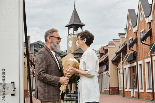 positive elderly couple in sunglasses, man looking at woman with flowers, summer, bouquet, romance