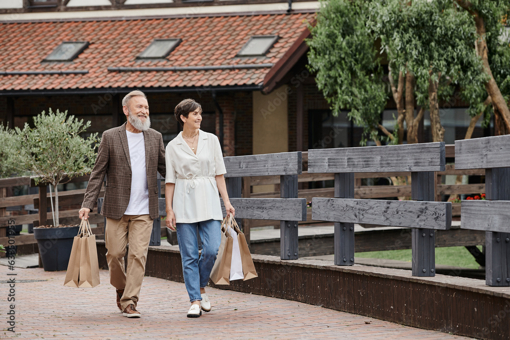 positive senior couple walking with shopping bags, elderly man hugging woman, walking together positive senior couple walking with shopping bags, elderly man hugging woman, walking together