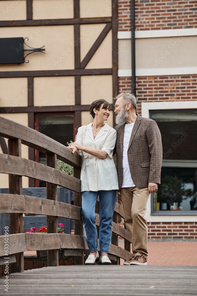 happy bearded man and woman looking at each other, senior couple, standing near bridge, romance happy bearded man and woman looking at each other, senior couple, standing near bridge, romance