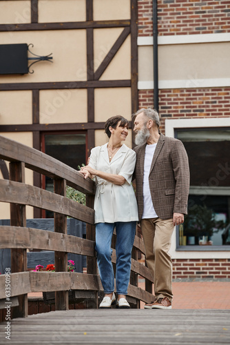 happy bearded man and woman looking at each other, senior couple, standing near bridge, romance