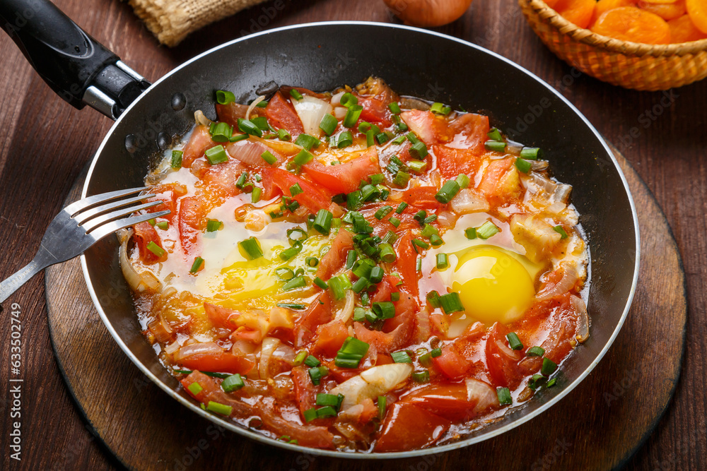 fresh shakshuka in a frying pan sprinkled with green onions on a laid Shabbat table. fresh shakshuka in a frying pan sprinkled with green onions on a laid Shabbat table.