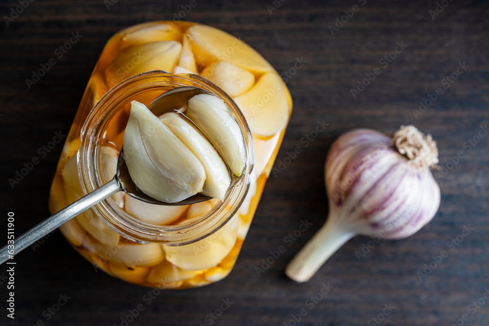 Spoon with sliced garlic cloves in honey over the opened honey jar, top