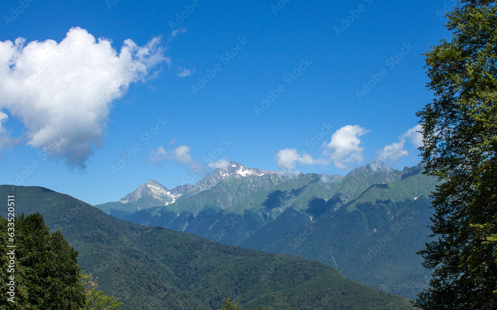 Naklejka premium beautiful panoramic mountain landscape with rock tops among green trees on a sunny summer day with white clouds and copy space in krasnaya polyana sochi russia